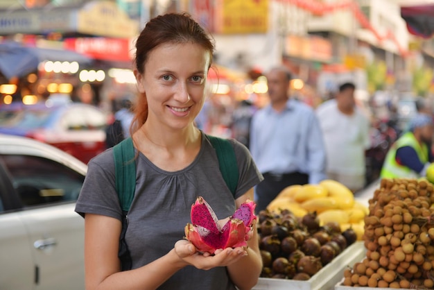 Cheerful Tourist woman tastes exotic dragon fruit on local Asian market