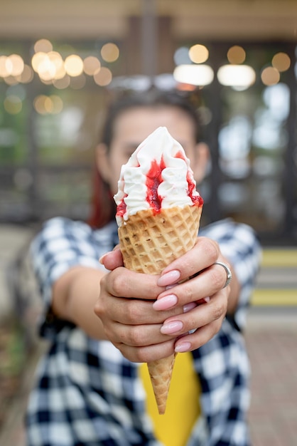 Cheerful trendy woman with red hair eating ice cream at street