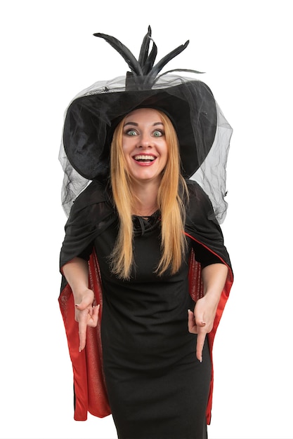 Photo cheerful woman in black witch hat and dress is pointing down halloween party white background young witch vertical frame