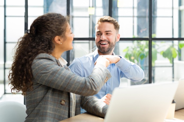 Cheerful woman bumping fist with male colleague making agreement cooperating