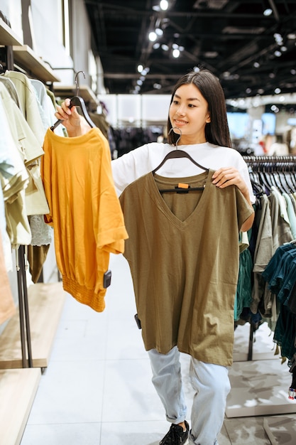 Cheerful woman choosing clothes in clothing store. Female person shopping in fashion boutique, shopaholic, shopper looking on garment