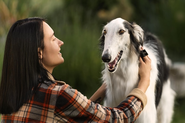 Cheerful woman combs her dog breed Russian wolfhound on the street