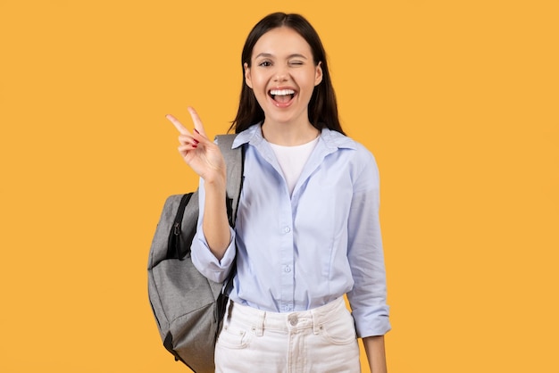 Cheerful woman doing peace sign on yellow background