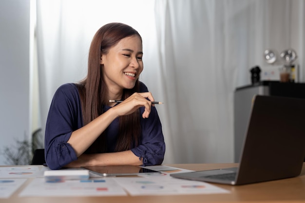 Cheerful woman freelancer working online on laptop sitting at desk at home looking at screen