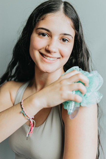 Cheerful woman holding and using an exfoliating sponge resting her face Young adult washing her body with bath loofah Washcloth body scrub closeup hands rub skin in bath Personal hygiene concept