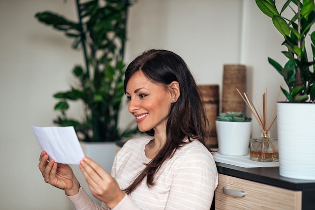 Cheerful woman looking at blank envelope at home.