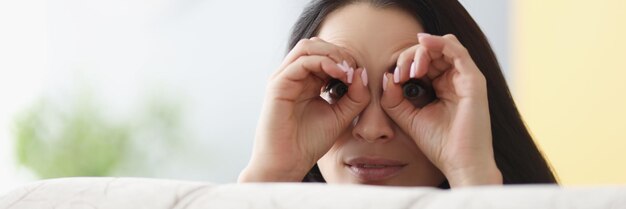 Cheerful woman peeking from behind sofa female hands make binoculars over eyes