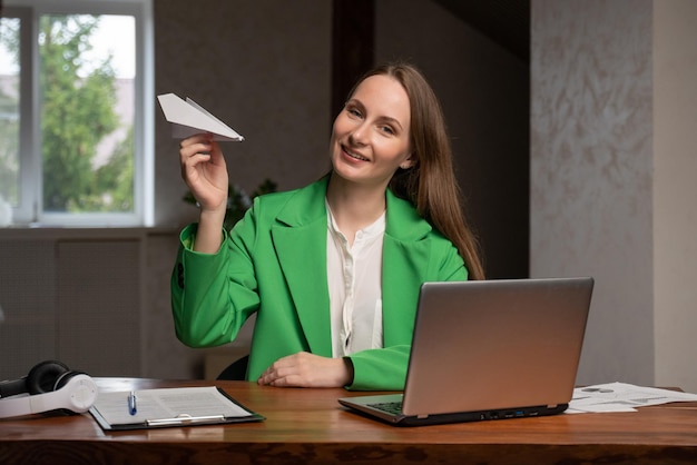 Cheerful woman plays with paper airplane sitting at table