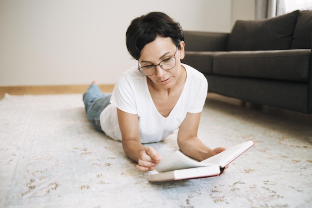 Cheerful woman reading paper book at home Brunette with short hair in casual clothes