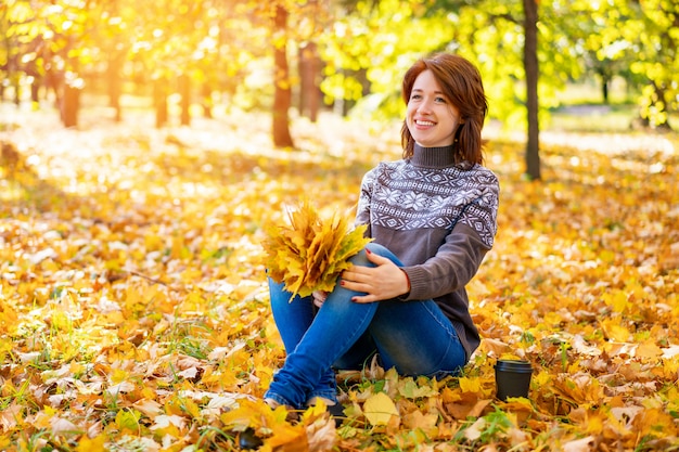 Cheerful woman sitting on yellow leaves