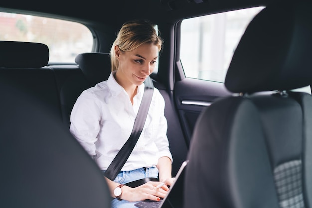 Cheerful woman smiling and thinking on back seat of car