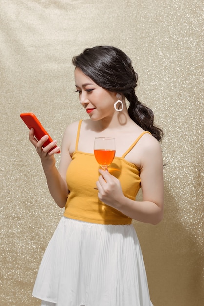 Cheerful woman texting message,  drinks champagne and holding phone over sparkles background