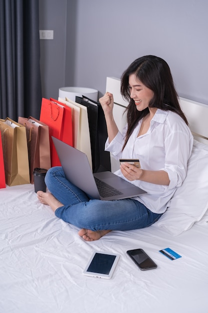 Cheerful woman using laptop computer to shopping online on bed