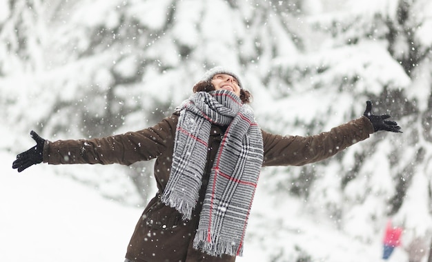 Cheerful woman in warm clothes enjoying the falling snow