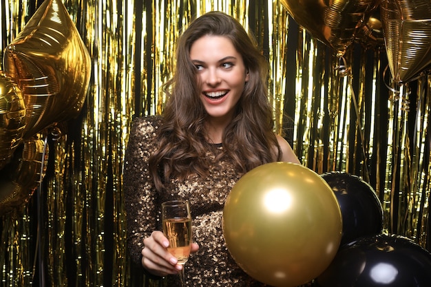 Cheerful woman with balloons laughing on gold background.