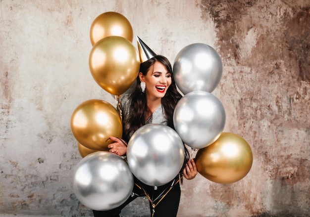 A cheerful woman with balloons laughs a young brunette with long hair celebrates her birthday helium balloons