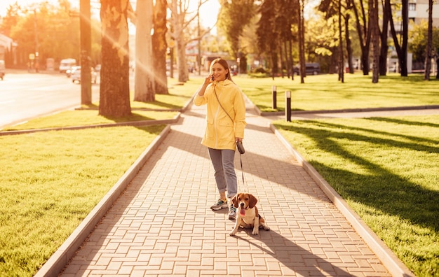 Cheerful woman with dog speaking on phone in park