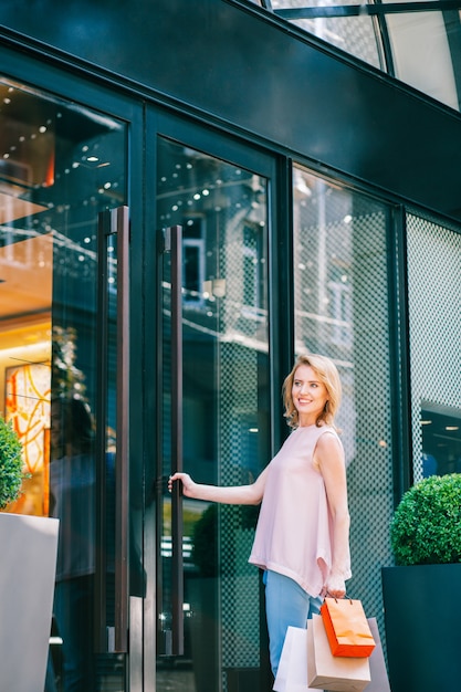 Photo cheerful woman with shopping bags looking away with a smile and entering a shop