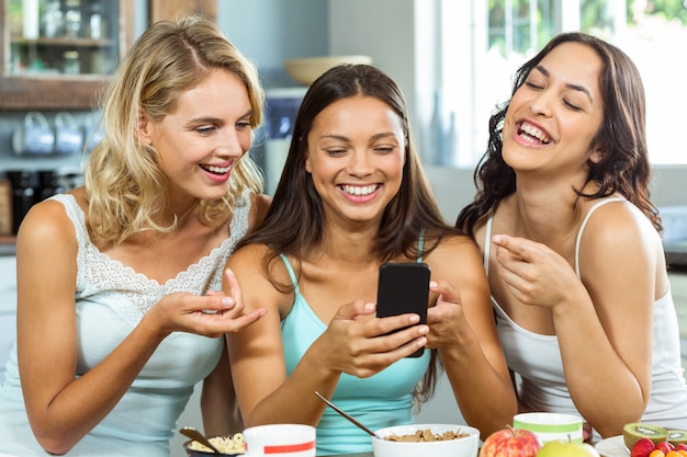 Cheerful women looking at pictures in mobile phone at home