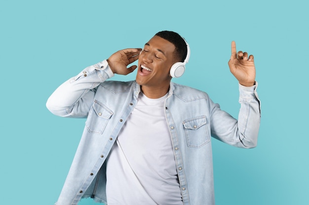 Cheerful young african american man in casual and wireless headphones sing song and enjoy music