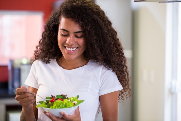 cheerful young afro american woman eating vegetable salad in home kitchen.