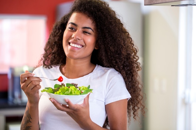 cheerful young afro american woman eating vegetable salad in home kitchen  