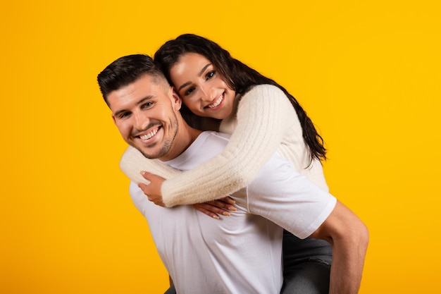 Cheerful young arab husband holding wife on his back enjoy tender moment have fun look at camera