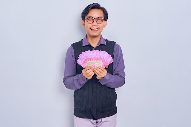 Cheerful young Asian businessman holding cash money in rupiah banknotes and looking at camera isolated on white background People lifestyle concept