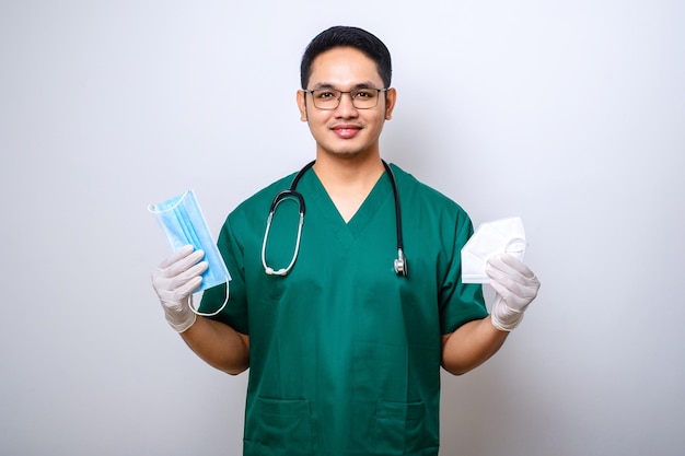 Cheerful young asian male doctor nurse in scrubs smiling and handing medical masks for patient safety