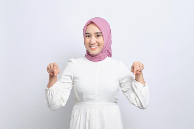 Cheerful young Asian Muslim woman pointing fingers down showing free place for advertisement isolated over white background