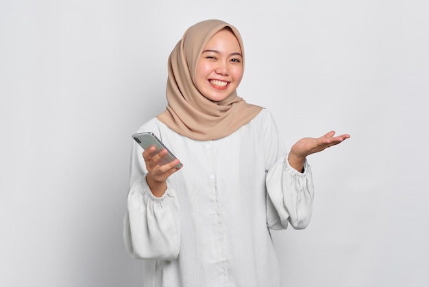 Cheerful young Asian Muslim woman using a mobile phone and celebrating success getting good news isolated over white background