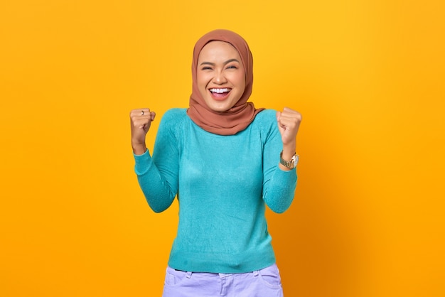 Cheerful young Asian woman celebrating victory, euphoric over achievement on yellow background