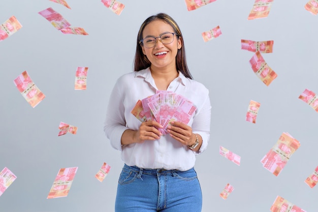 Cheerful young Asian woman holding money banknotes isolated over white background