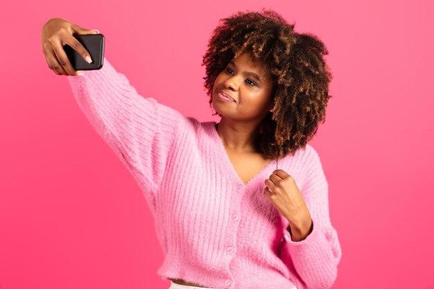 Cheerful young black curly lady student in casual takes selfie on smartphone shooting video for blog