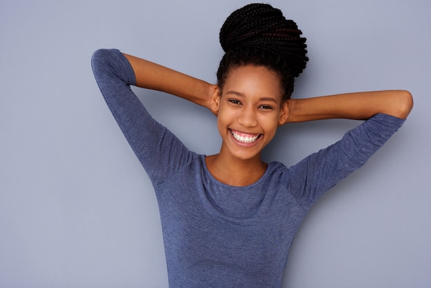 Cheerful young black girl with hands behind head smiling on gray background