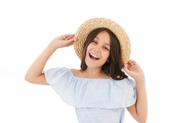 Cheerful young brunette girl in dress and straw hat posing on white