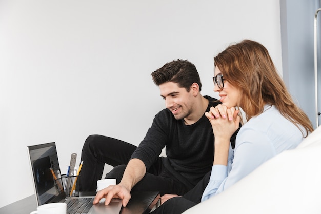 Cheerful young couple of colleagues working together at the office, co-working teamwork concept, using laptop