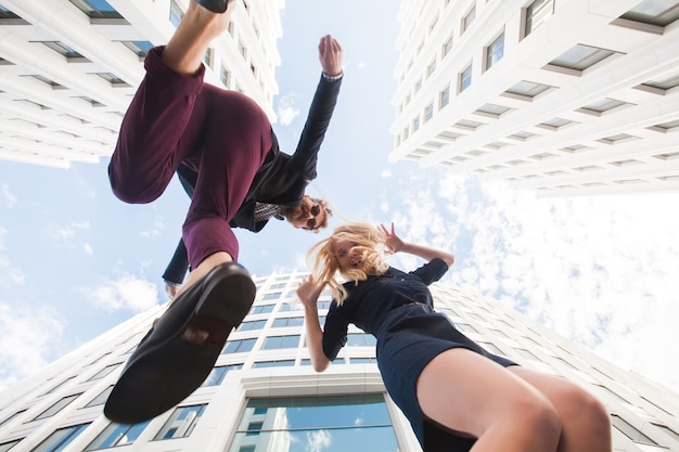 Cheerful young couple fooling around, jumping on the background of the building. Bottom view