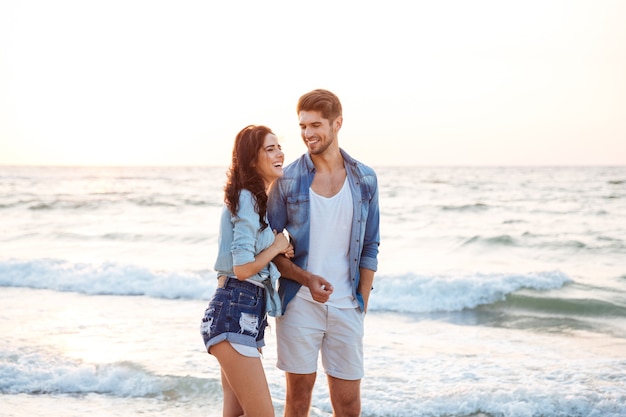 Cheerful young couple laughing and walking on the beach