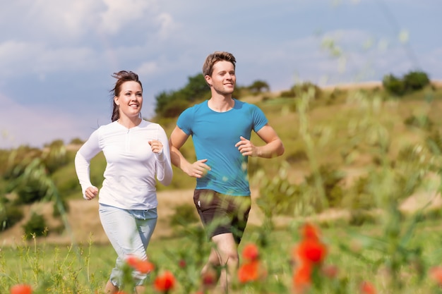 Cheerful young couple running between flowers in a sunny meadow