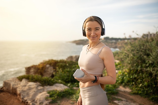 Cheerful young european lady athlete in sportswear and headphones use smartphone enjoys music for