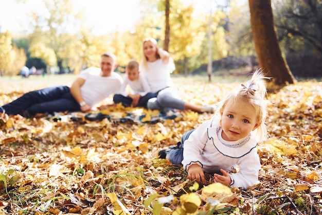 Cheerful young family lying down on the ground and have a rest in an autumn park together.