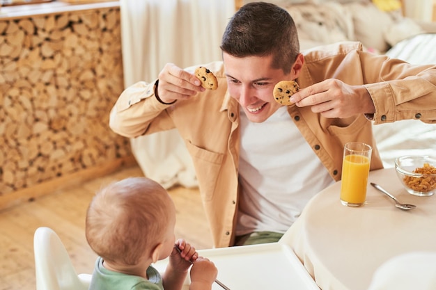 Cheerful young father entertains the kid during breakfast