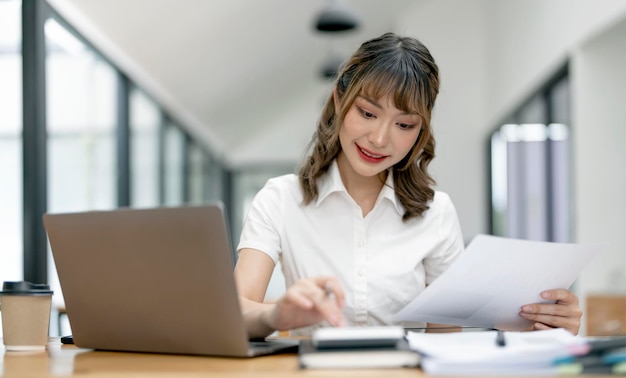 Cheerful young female businesswoman or student smiling and working on computer laptop at office