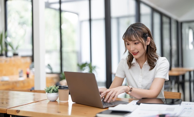 Cheerful young female businesswoman or student smiling and working on computer laptop at office