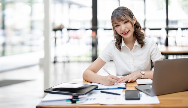 Cheerful young female businesswoman or student smiling and working on computer laptop at office