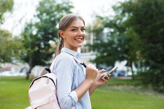 Cheerful young girl carrying backpack spending time