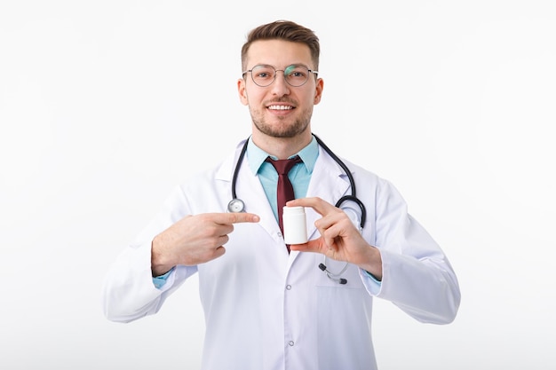 A cheerful young male doctor holds a medicine in his hand and points to it with a gesture