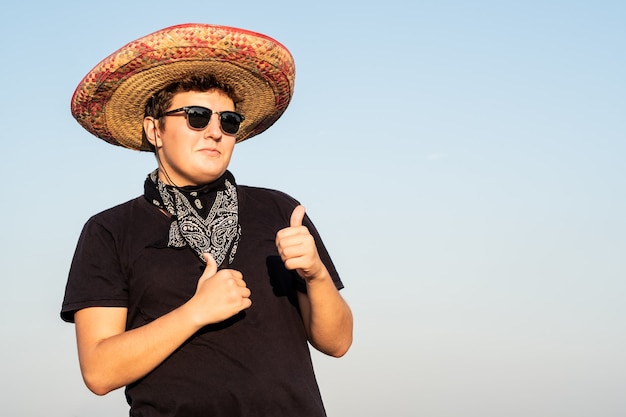 Cheerful young male person in sombrero in clear sky background. Mexico independence festive concept of partying man wearing national mexican hat and western style bandana