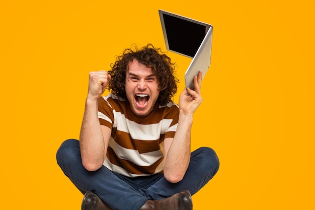 Cheerful young male winner with laptop yelling